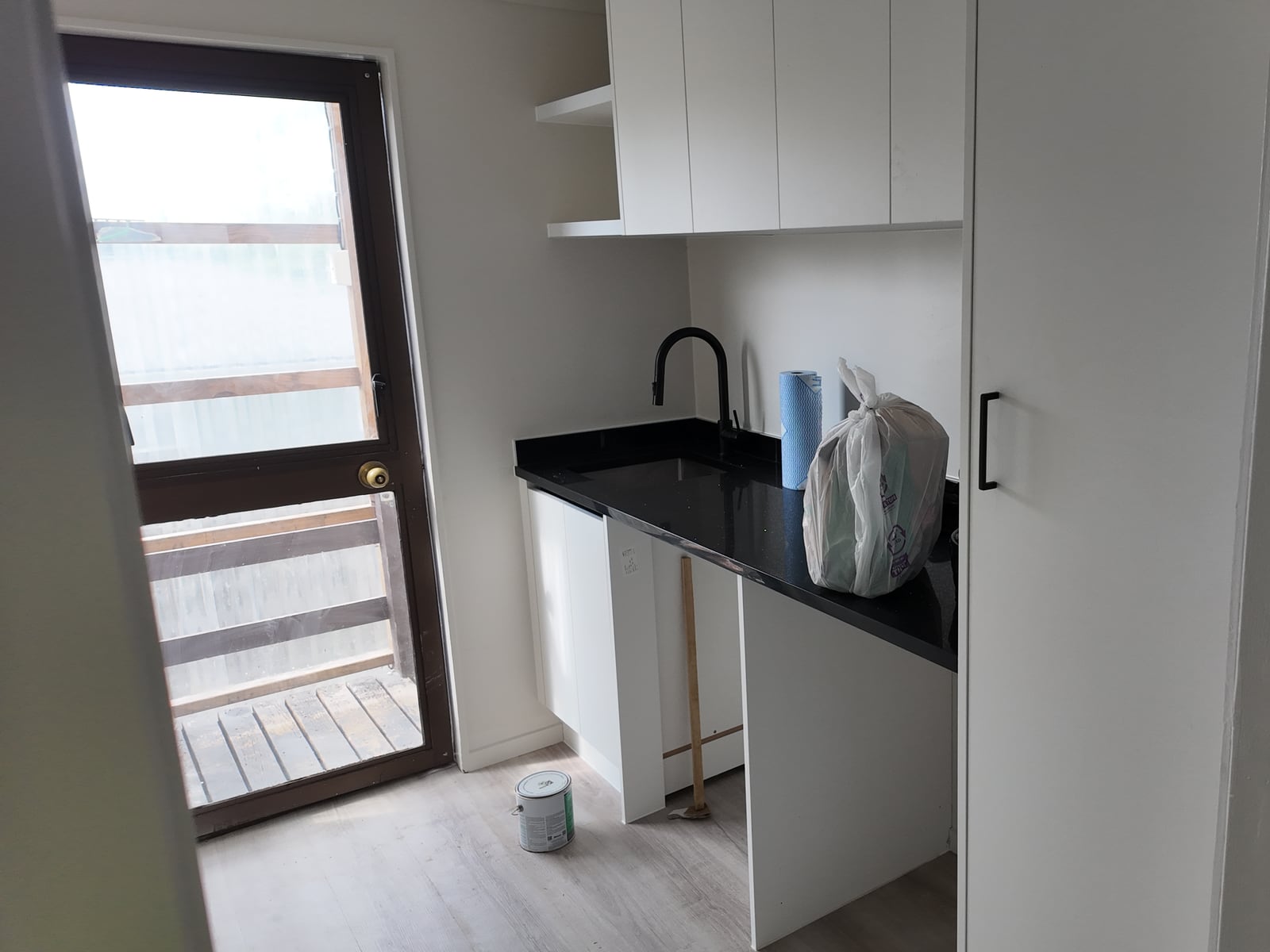 Renovated laundry with an integrated tub, white cabinetry and black worktop